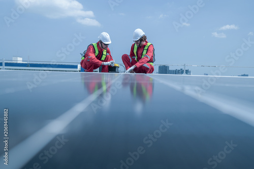 Fotografi Pair of technicians in red protective suits stride across rows of photovoltaic panels on a city rooftop, showing green technology, inspection and maintenance on a rooftop photovoltaic array