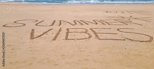 Summer vibes message written in sand on beach