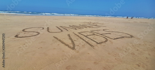 Summer vibes lettering drawn in sand on beach