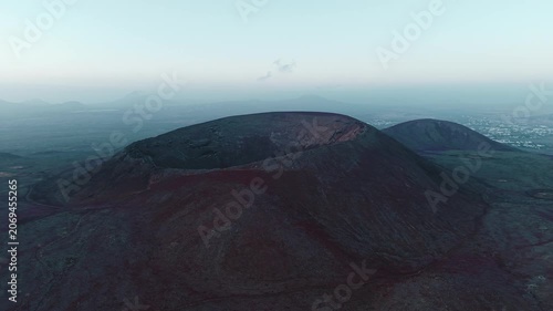 Drone flight approaching a massive volcanic crater rising from the barren landscape of Fuerteventura, Canary Islands, Spain. Dramatic geological formation surrounded by ancient lava fields