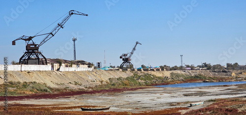 Fotografie Former port cranes and abandoned boats on the exposed seabed near Aralsk, Kazakhstan