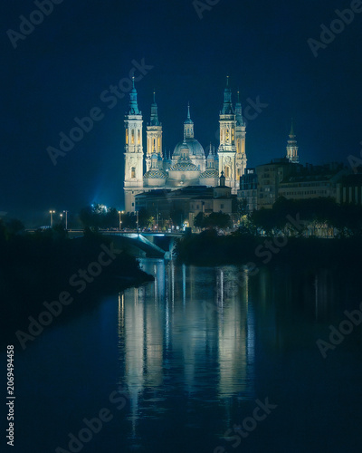 Illuminated Basilica del Pilar cathedral with reflection on Ebro river at night in Zaragoza, Spain