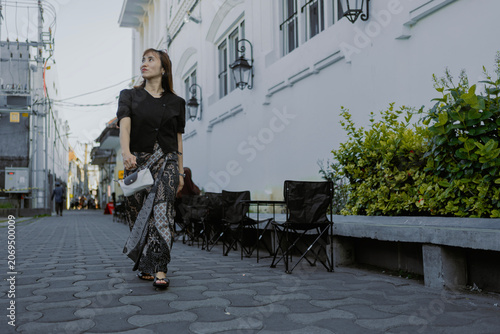 Fashionable adult Asian woman in casual black shirt and batik bottom walking in the urban alley city street.