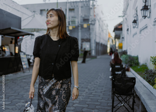 Fashionable adult Asian woman in casual black shirt and batik bottom walking in the urban alley city street.