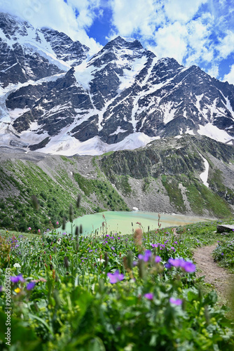 Obraz na płótnie Emerald mountain lake in the Caucasus Mountains during summer, surrounded by greenery with glacier-covered peaks and the Semerka glacier in the background