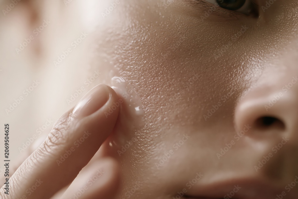 Fototapeta premium Close-up macro shot of a finger applying a clear cosmetic serum or moisturizer to textured skin.