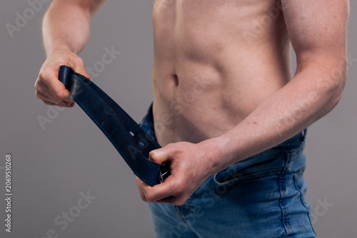 Foto A muscular man in blue classic jeans with a bare torso is holding a belt