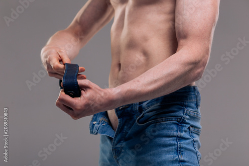 Konstfotografi A muscular man in blue classic jeans with a bare torso is holding a belt