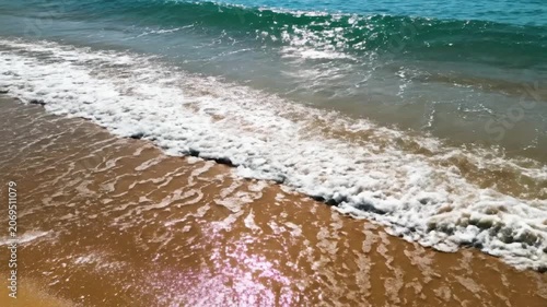 Gentle ocean waves wash over a golden sandy beach under bright sunlight