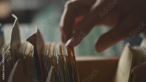 Female fingers browsing through old paper index card catalog in archival cabinet drawer, slow motion 4K