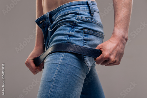 Cuadro en lienzo A muscular man in blue classic jeans with a bare torso is holding a belt