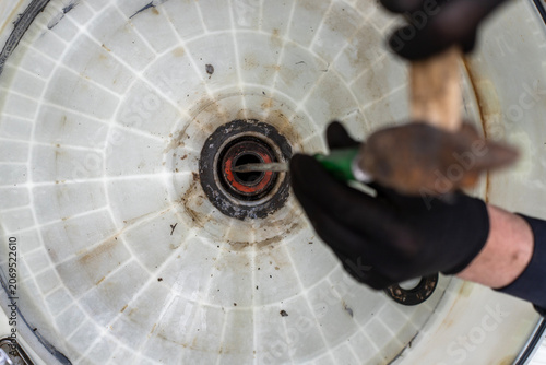 Billede på lærred Overhead view of a technician using a hammer and a punch tool to knock out a worn, dirty ball bearing from a disassembled plastic washing machine tub during repair process