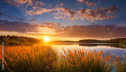 A Beautiful Sunset Over A Lake With Tall Grasses In The Foreground