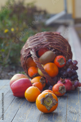 Vertical shot of autumn fruits spilling from a wicker basket on wooden surface.