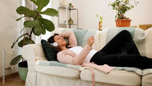 Fotografie Woman lying down on a cozy sofa, enjoying music with headphones, finding peace a