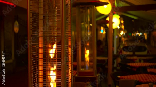 Gas patio heater burning at night on an empty restaurant terrace. Outdoor gas heater providing warmth and ambiance on a chilly evening at a cafe terrace, with decorative lights