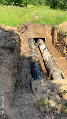 Pipeline accident: hot water jets gushing from a rusted pipe in a dug trench
