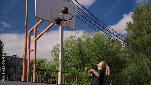 Person practices shooting basketball at urban court on a clear day under blue sky