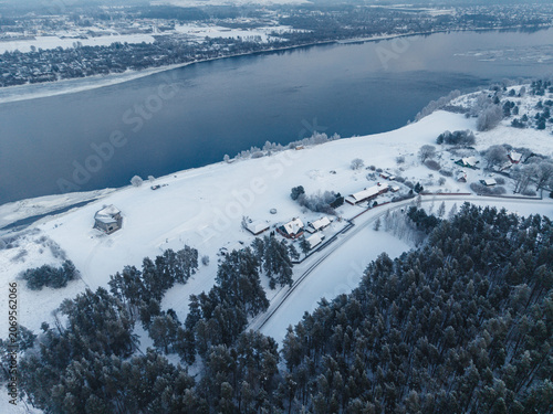 Aerial view of Doles sala on the Daugava river featuring snow-covered forests and houses in the winter landscape of Salaspils pagasts, Salaspils novads, Latvia.