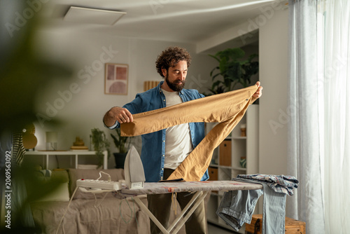 Foto Man ironing casual pants in domestic setting living room