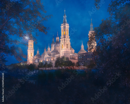 A stunning architectural shot of the Cathedral-Basilica of Our Lady of the Pillar in Zaragoza, Spain, illuminated during the blue hour. The grand baroque building with its majestic towers