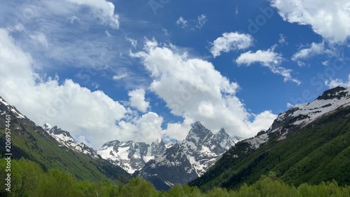 Stunning mountain scenery featuring snow-covered peaks and vibrant green valleys beneath a clear blue sky filled with white clouds