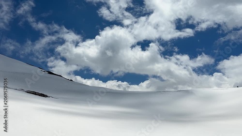 Snow-covered hills stretch across the landscape, with fluffy clouds drifting in a bright blue sky, creating a tranquil winter scene