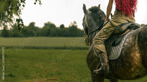 Foto Woman with vibrant red hair rides a horse through a grassy field