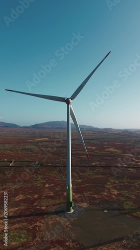 Drone vertical shot of a wind turbine rising above volcanic terrain in Fuerteventura, Canary Islands, Spain. Renewable energy structure surrounded by arid landscape.