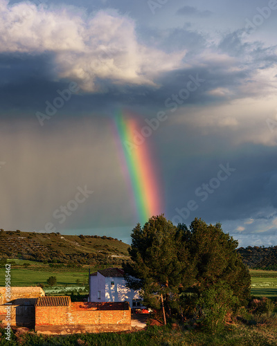 Vibrant rainbow over a rural countryside landscape under a stormy sky ,A spectacular landscape shot of a bright and colorful rainbow stretching down from dark, dramatic storm clouds onto a rural 