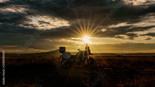 Adventure motorcycle silhouette against a dramatic sunset with sunbeams, A powerful silhouette of an adventure touring motorcycle parked in a rural field during a breathtaking sunset. 