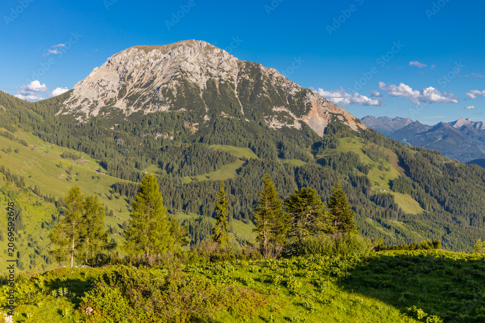 Fototapeta premium Rocky mountain summit in the Austrian Alps near Salzburg, Austria. Jagged cliffs, steep slopes, and rugged alpine terrain dominate the landscape, while surrounding mountain ranges stretch toward the h