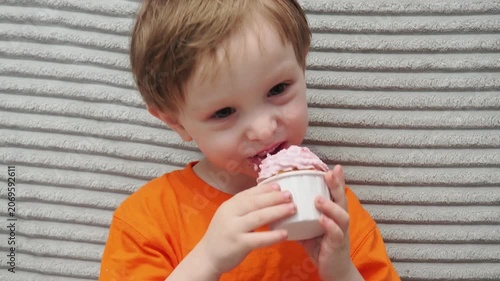 Child Eating, cupcake for dessert, sweet treat or sugar snack . Boy Bite, tasting vanilla cake with pink cream on top, hungry and enjoy delicious food. Happy childhood: a child enjoys a sweet treat