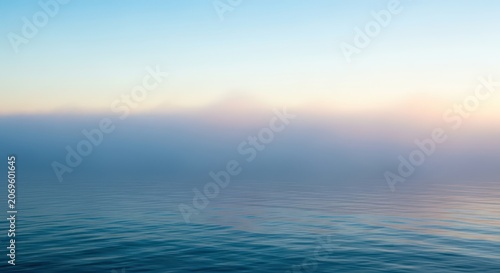 A dense layer of fog hangs low over the surface of the calm, cold ocean water creating a mysterious atmosphere at dawn light, weather, empty, natural