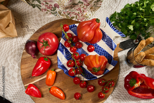 Foto Rustic Mediterranean food table with fresh tomatoes, cherry tomatoes, red peppers, basil, breadsticks and a wicker basket with floral cloth