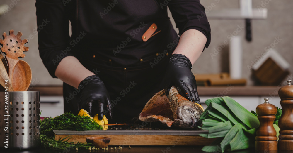 Obraz premium Private chef hands opening raw stuffed trout carcass on wooden board. Gourmet culinary preparation and premium catering service concept.