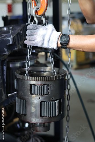 Obraz na plátne Close-up of a mechanic hand lifting a heavy transmission planetary gear carrier assembly using chains and a hook in a workshop