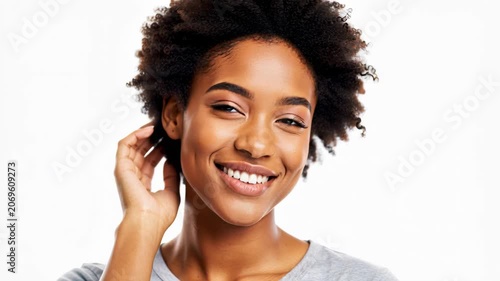 Joyful Smile: A young Black woman with natural afro hair beams with a radiant smile, her hand gently touching her hair, exuding confidence and happiness.