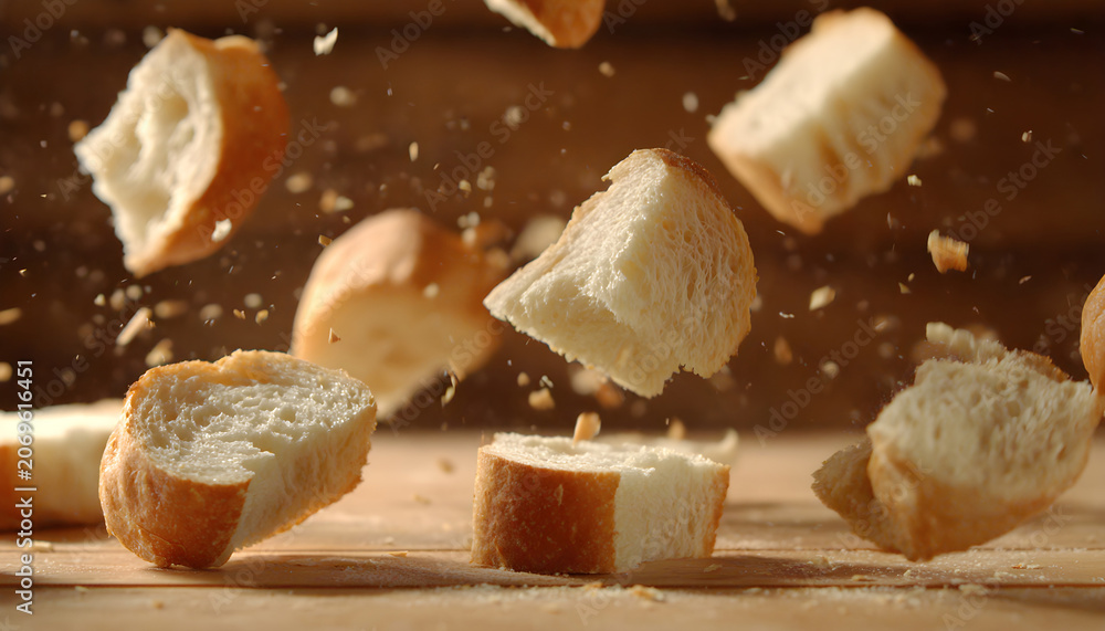 Fototapeta premium Super slow motion pieces of fresh bread fall on the table. On a wooden background