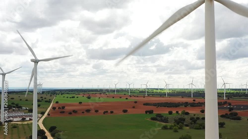 Witness the beauty of towering wind turbines gracefully spinning against a backdrop of vibrant farmland and expansive skies. A stunning view of renewable energy in motion.
