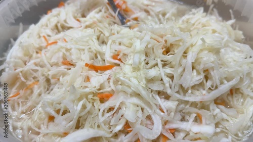 Fresh sauerkraut with carrot shreds displayed in transparent plastic container on market counter, market vendor presenting
