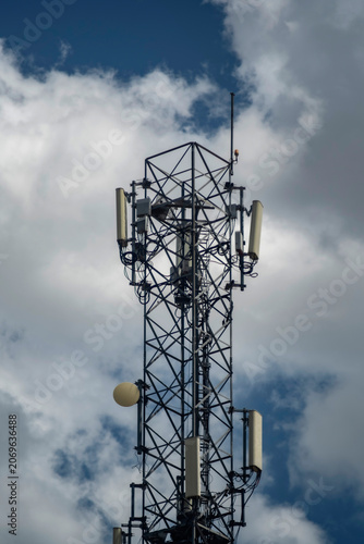 Low-angle shot of a telecommunications tower with 5G antennas and transmission equipment against a blue sky with clouds. Symbolizing global digital connectivity and network infrastructure.