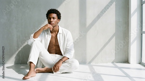 Young man in white attire sitting gracefully in a bright and minimalistic space
