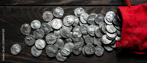 Tableau sur toile Ancient silver coins spilling out of a red pouch onto a dark rustic wooden table
