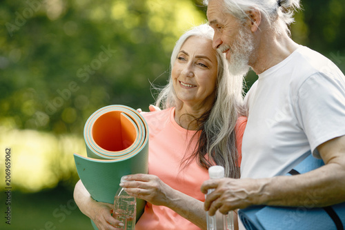 Senior couple with exercise mats standing at park and hugging