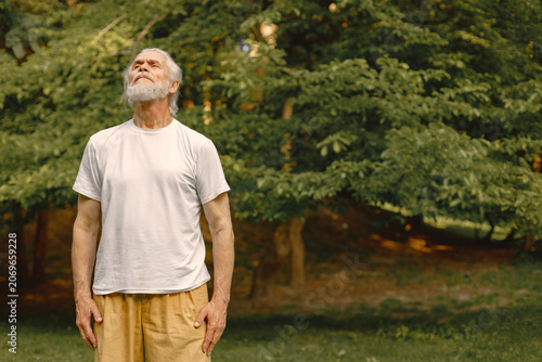 Senior man standing at summer park and doing excercises