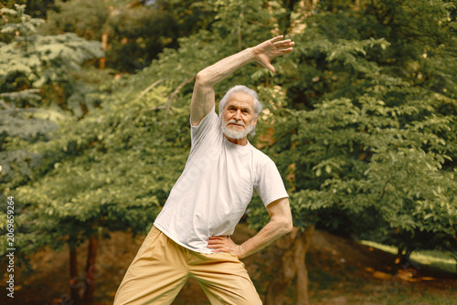Senior man standing at summer park and doing excercises