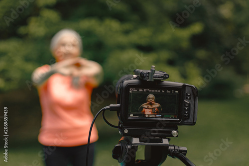 Cropped photo of camera shooting a senior woman standing at park and doing excercises