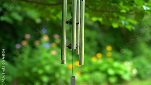 Metal wind chimes hang from a tree branch in a lush green garden