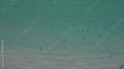 Tranquil swimmers explore vibrant turquoise sea with sandy shoreline; enjoying serene coastal scene amidst shipping containers for wellness, travel, and lifestyle photography concepts.